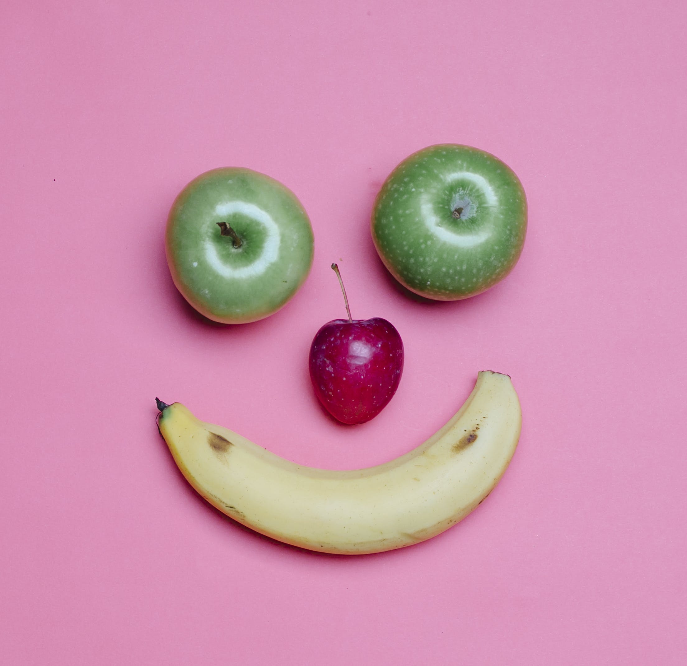Top view of fresh ripe banana and green and red apples arranged as smile on pink background